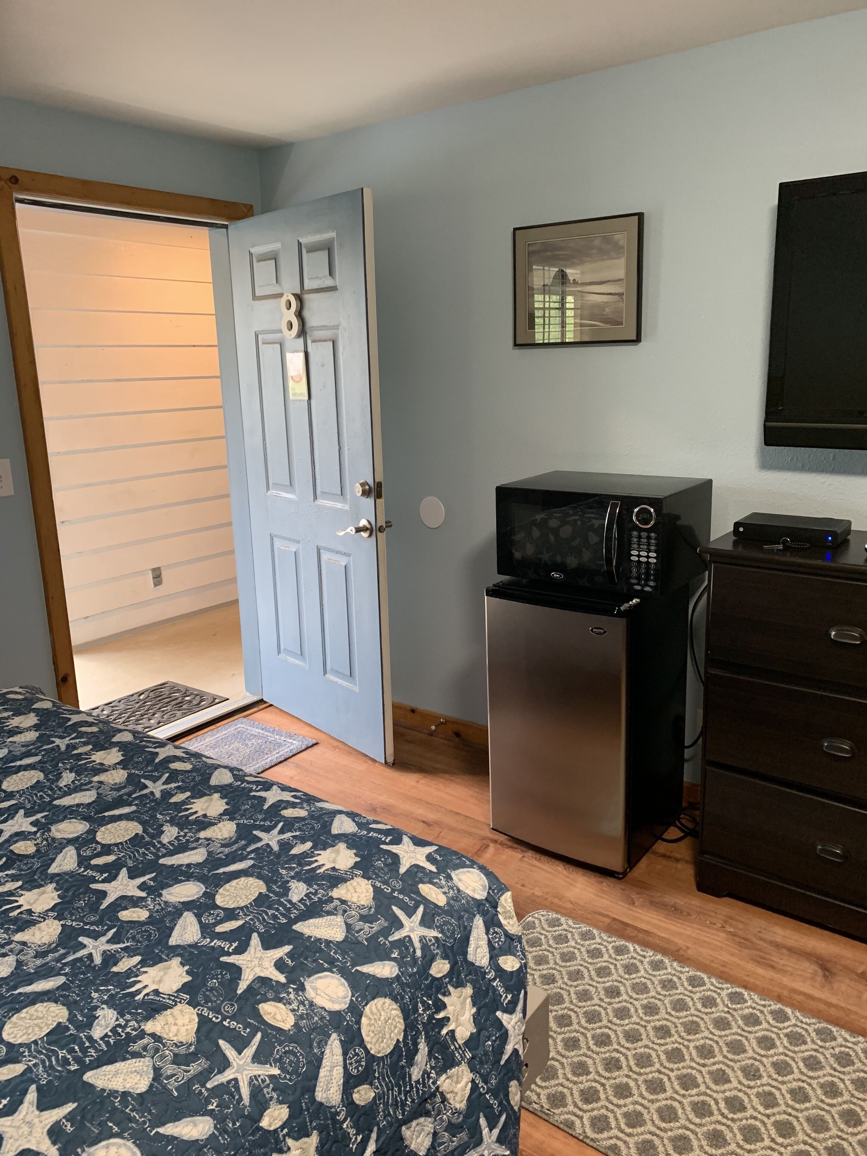 Un dormitorio con cama, microondas, cómoda y una puerta con un número.