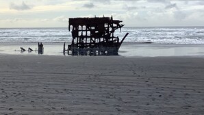 A beach with a large, rusted shipwreck in the water. - South Jetty Inn (Hammond)