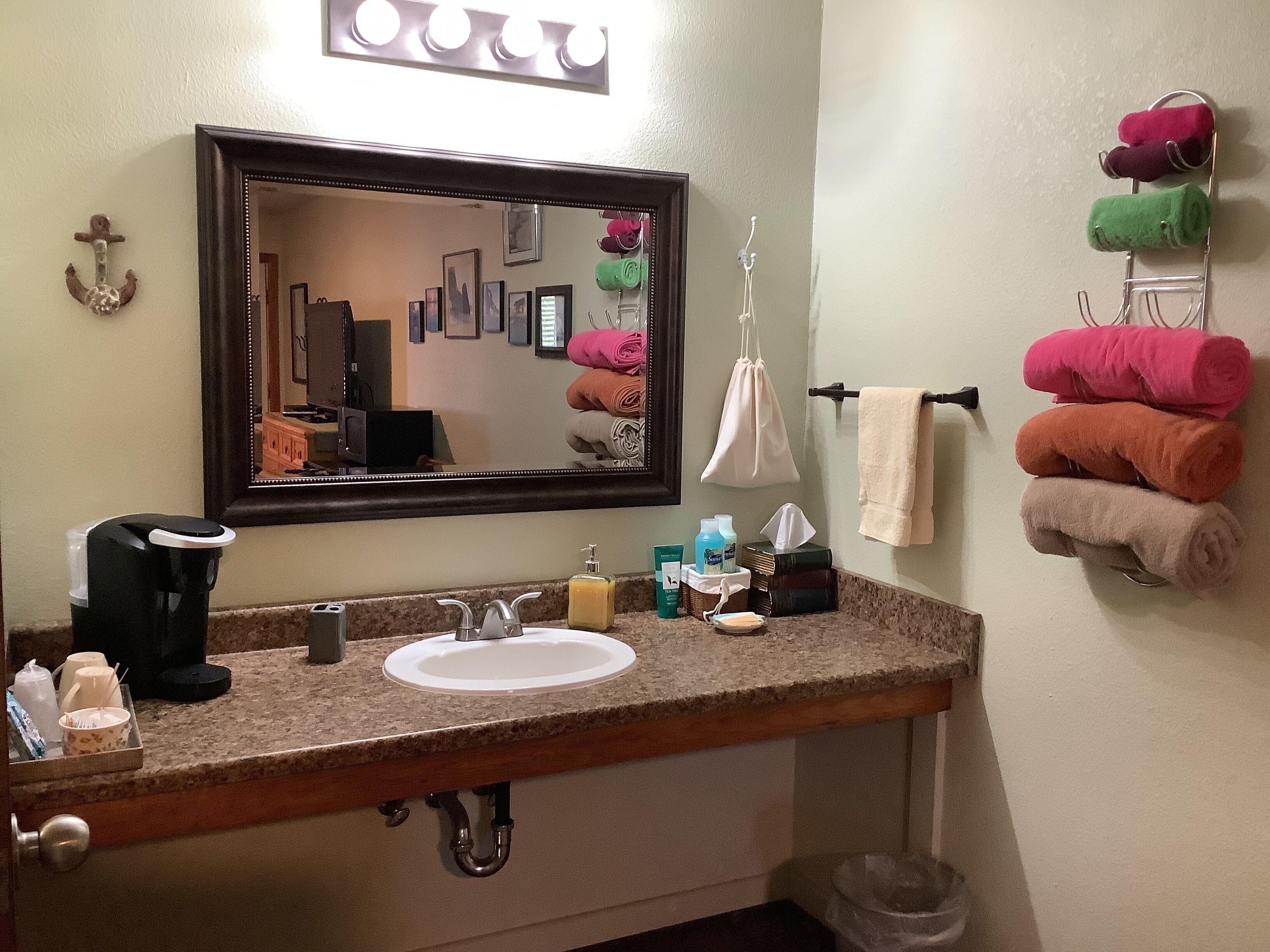 A bathroom with a sink, mirror, towel rack, and various toiletries.