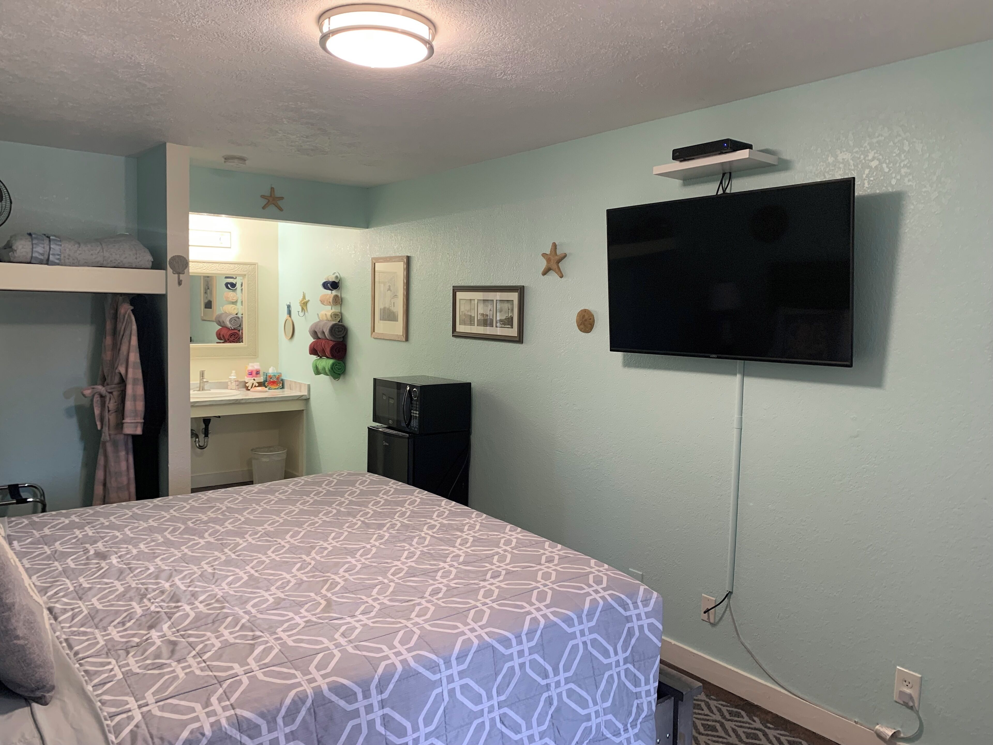 Een slaapkamer met een bed, een televisie, een kleine kitchenette en een badkamer.