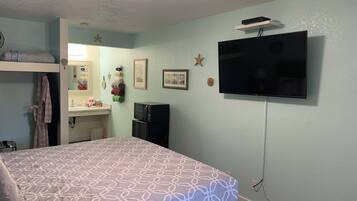 Een slaapkamer met een bed, een televisie, een kleine kitchenette en een badkamer.