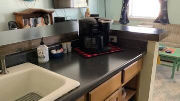 A kitchen with a coffee maker, a sink, and a window with curtains.