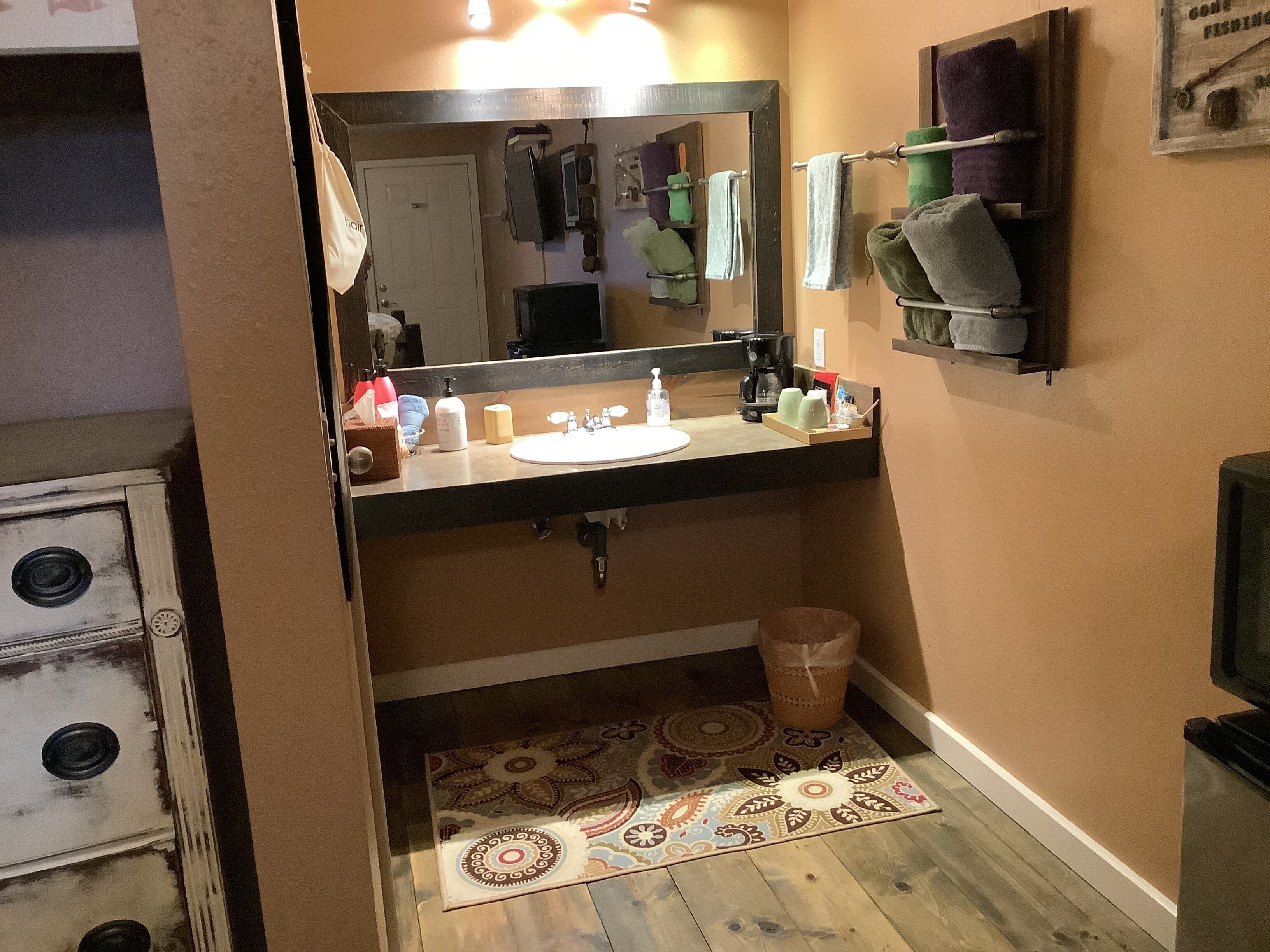 Un bany amb un lavabo, un mirall, un suport per a tovalloles i una catifa amb dibuixos a terra.