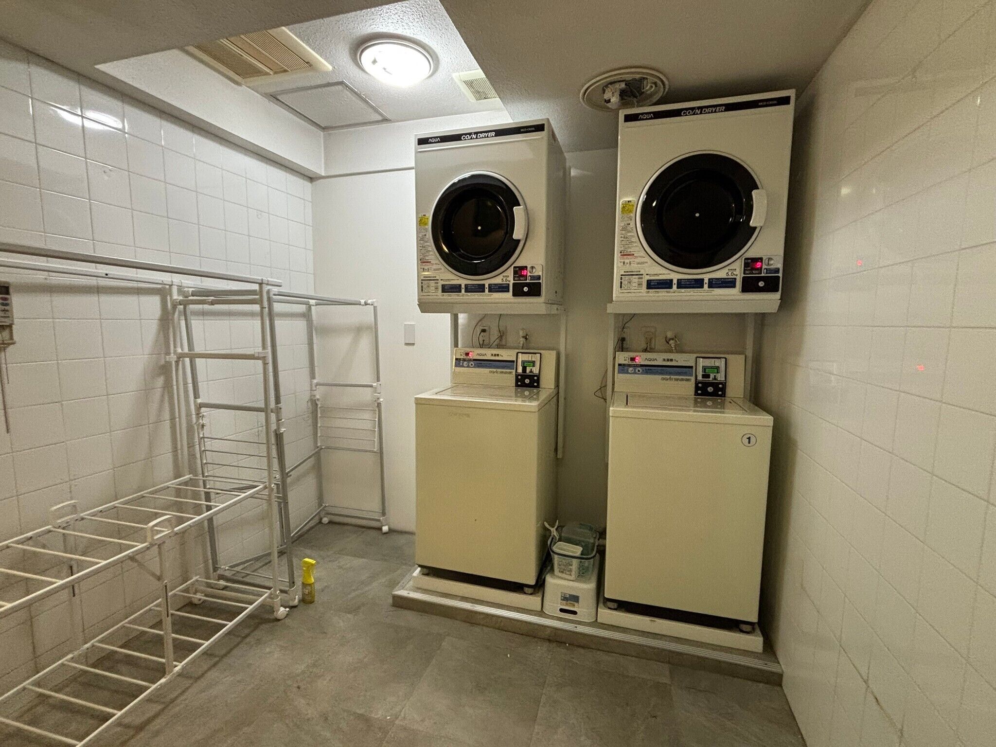 A laundry room with two front-loading washing machines and a metal drying rack.