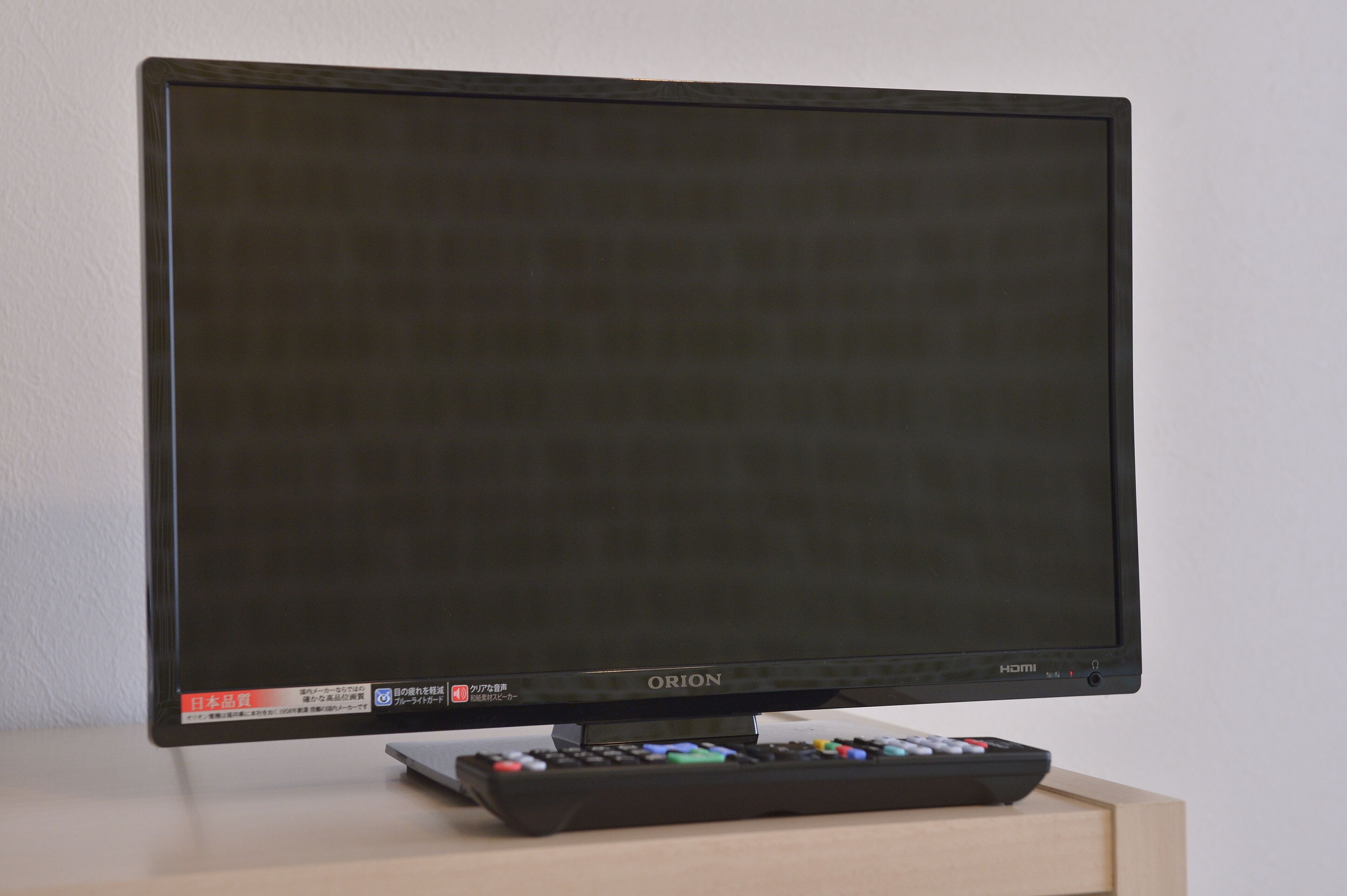 A flat-screen TV with a remote control on a wooden stand.