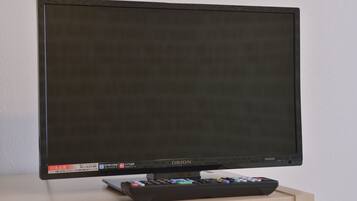 A flat-screen TV with a remote control on a wooden stand.