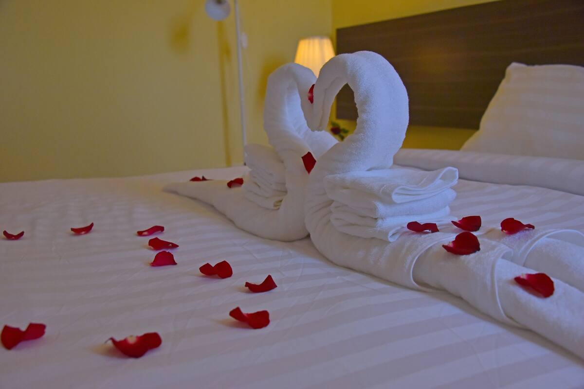 Een netjes opgemaakt bed met een zwaan van handdoeken en losse rozenblaadjes.