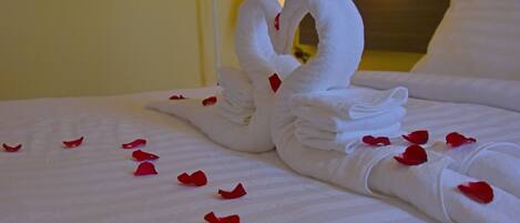 Una cama bien arreglada con una toalla doblada en forma de cisne y pétalos de rosa esparcidos.