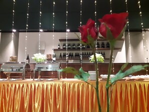 A banquet table with a golden drape, wine bottles on shelves in the background, and a red rose in the foreground.