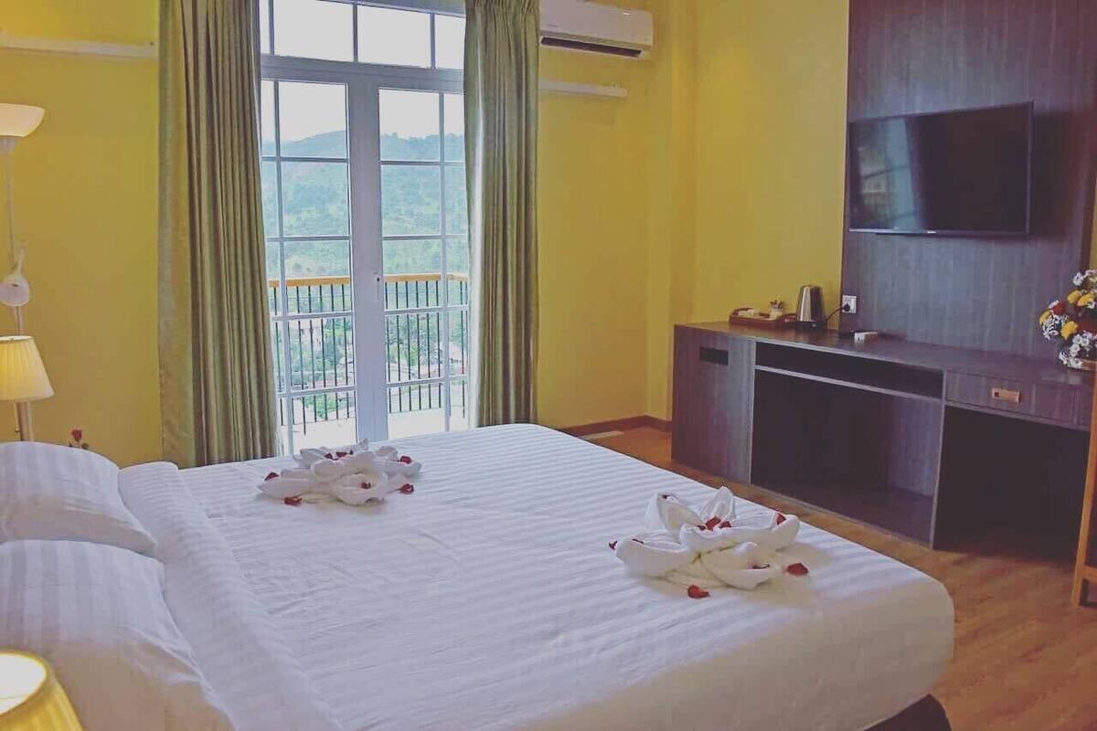 Een hotelkamer met een bed, een televisie en een balkon met uitzicht op groen.
