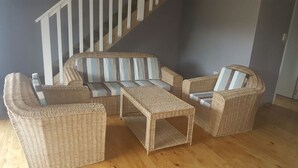 Een rieten zithoek met gestreepte kussens, een bijpassende fauteuil en een kleine tafel, alles op een houten vloer.
