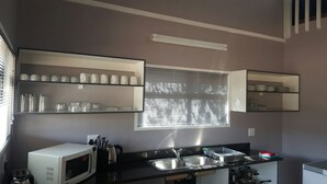 Een kleine keuken met een magnetron, spoelbak en planken voor servies.