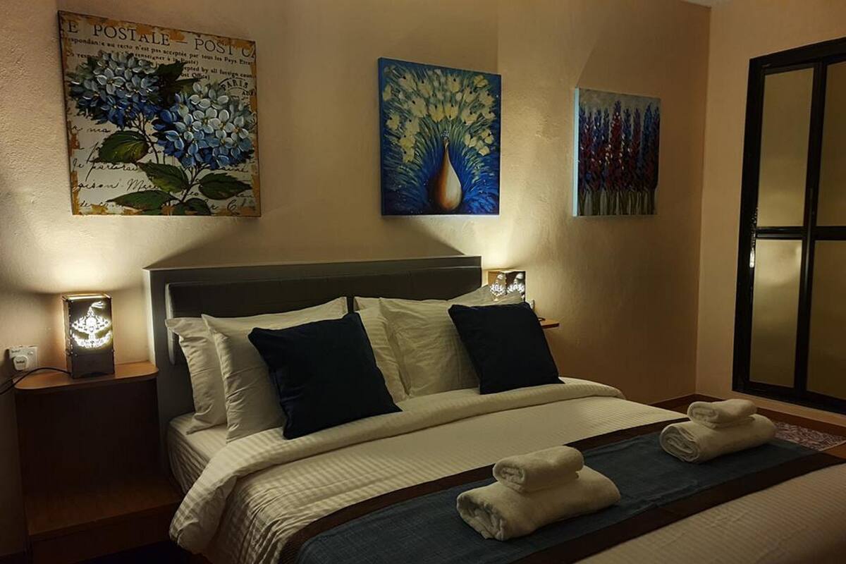 Un lit bien fait, avec une literie blanche et bleu foncé, deux tableaux accrochés au mur et une table de chevet avec une lampe.
