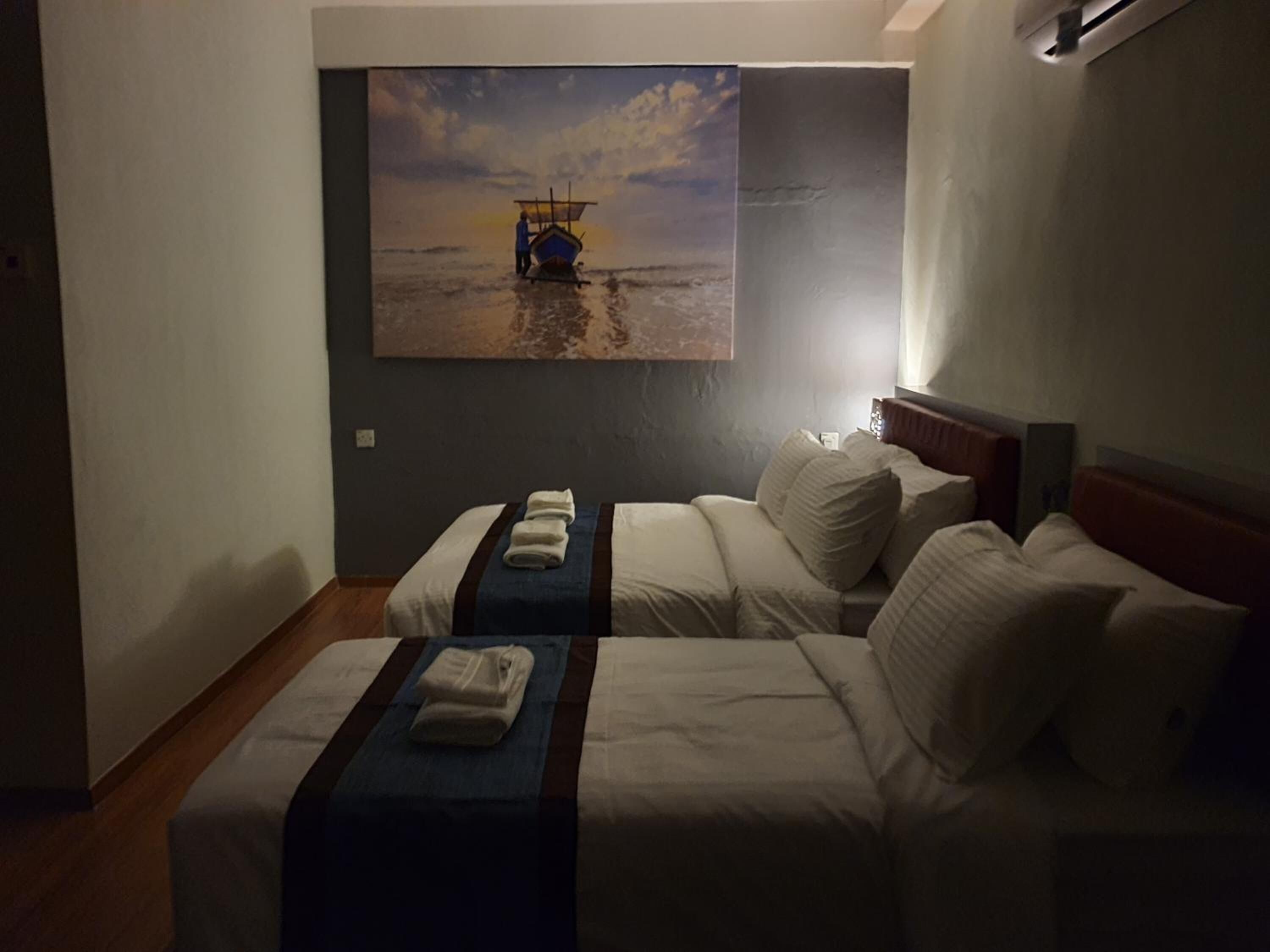 Ein Hotelzimmer mit zwei Betten, einem Bild von einem Boot am Strand und einem Holzboden.
