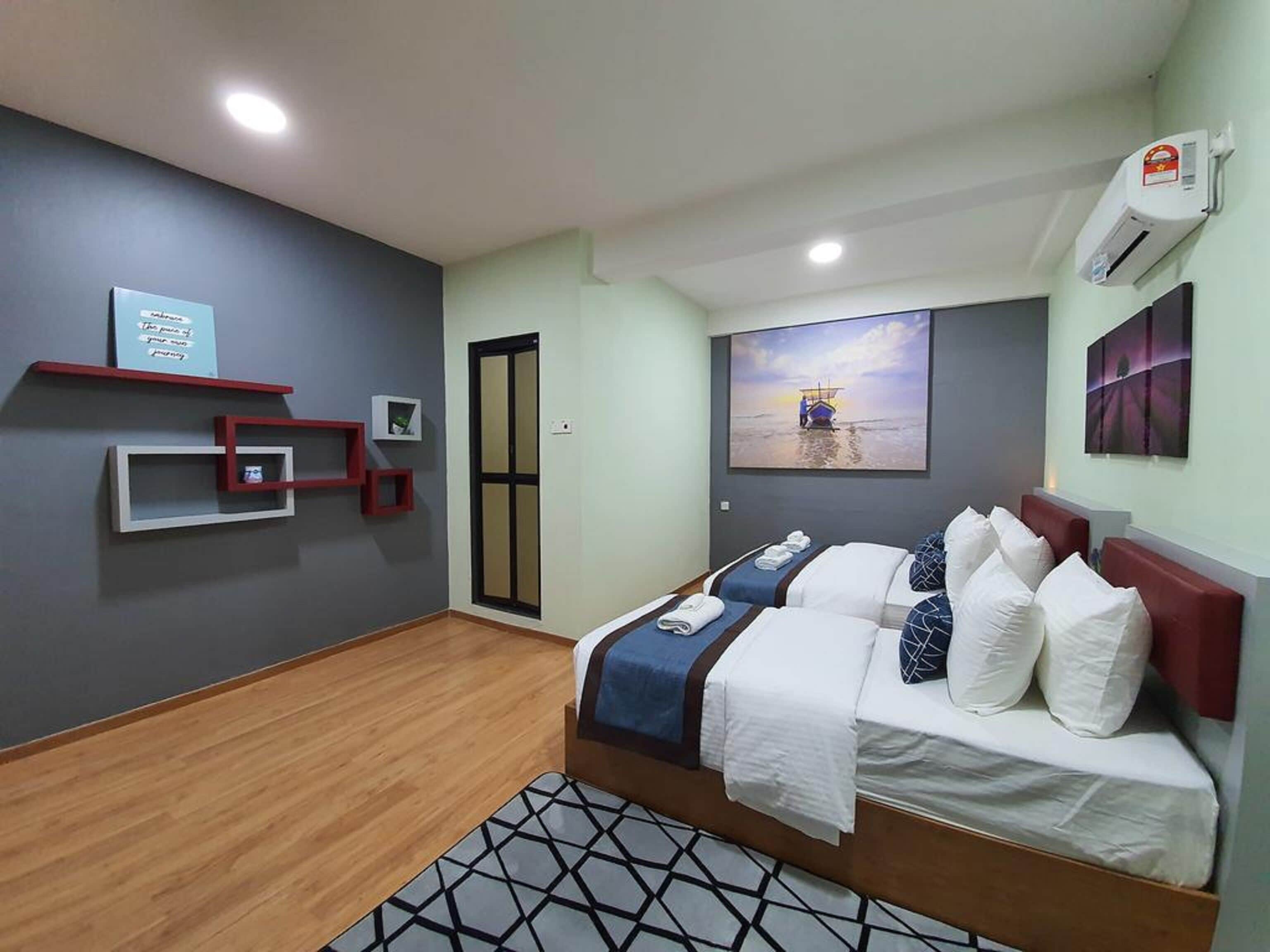 Habitación de hotel con cama, aire acondicionado de pared, un cuadro y una pequeña estantería con objetos decorativos.
