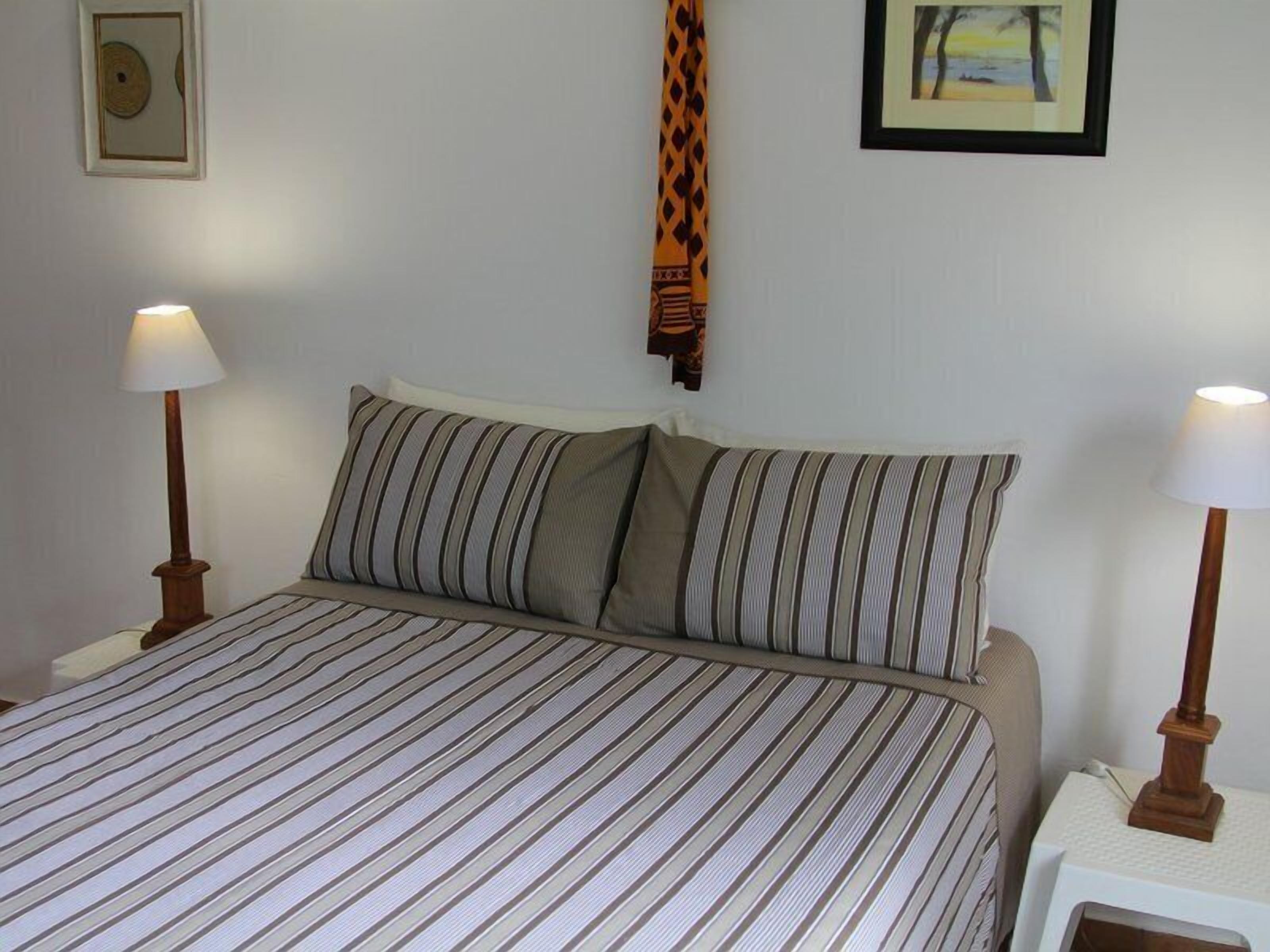 Una cama con ropa de cama a rayas, dos lámparas de noche y un cuadro en la pared.