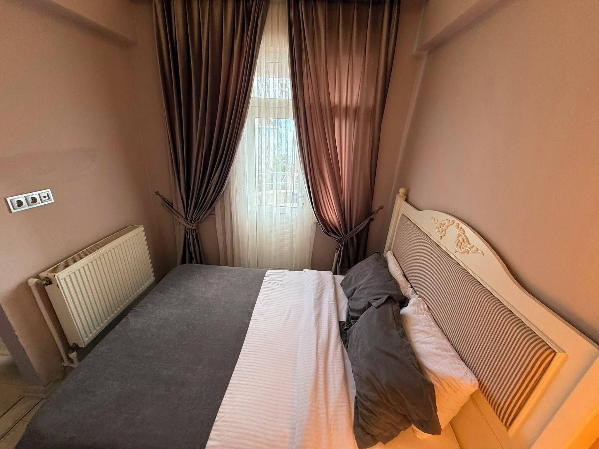 Un dormitorio con cama, cortinas, un radiador y una ventana.