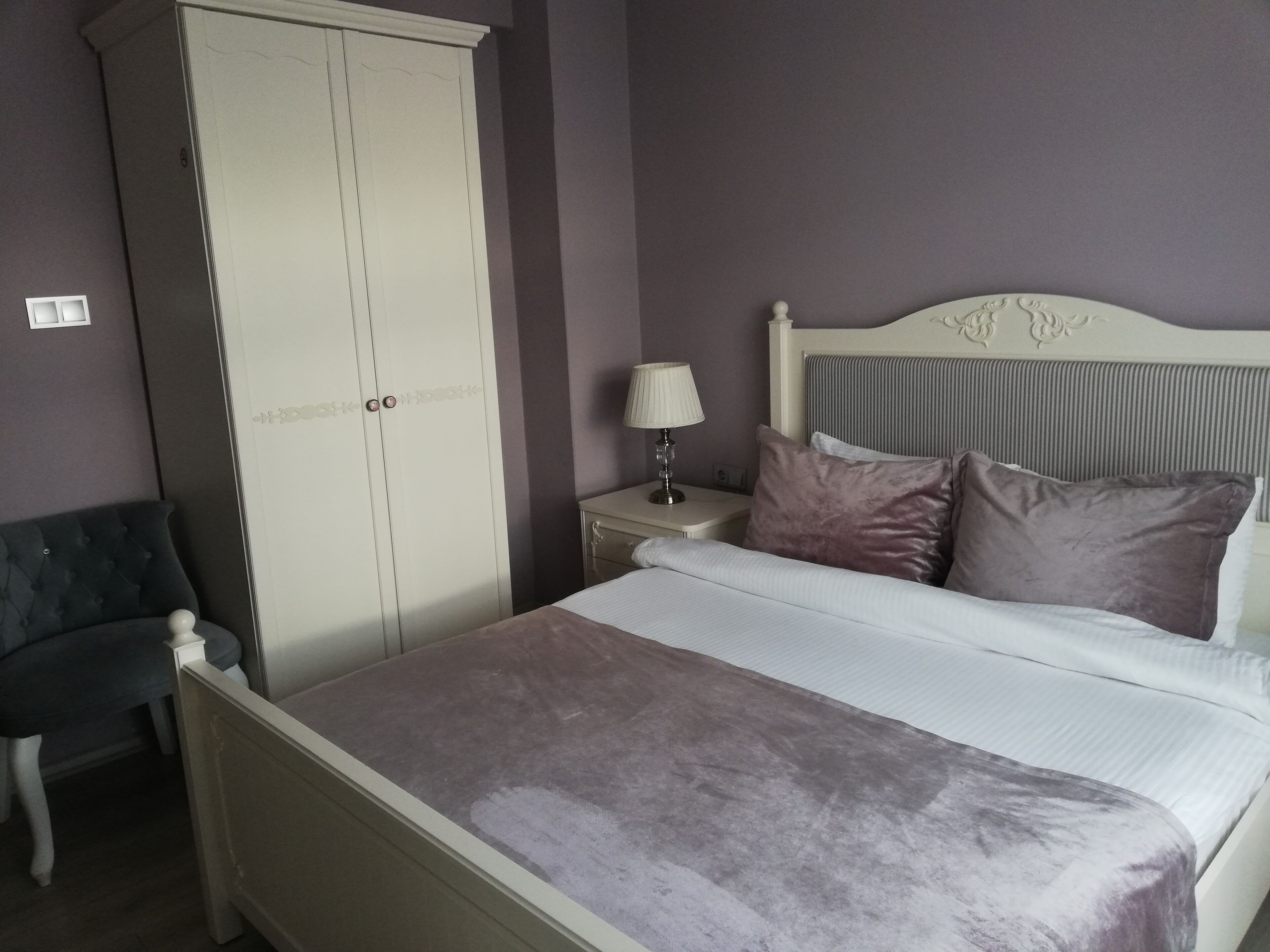 Ein Schlafzimmer mit Bett, Nachttisch, Lampe, Kleiderschrank und Stuhl.