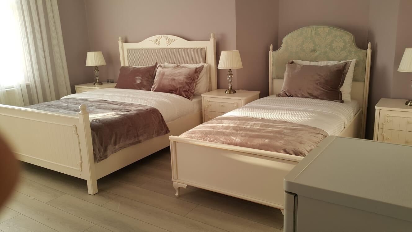 Un dormitorio con dos camas, cada una con una mesita de noche y una lámpara. El piso es de madera y hay una ventana con cortinas.