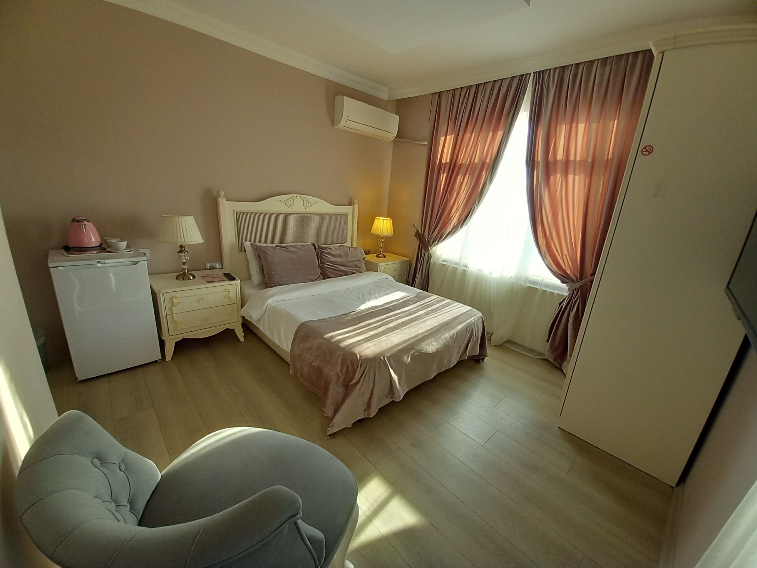 A hotel room with a bed, bedside tables, a desk with a lamp, a chair, and a wardrobe.