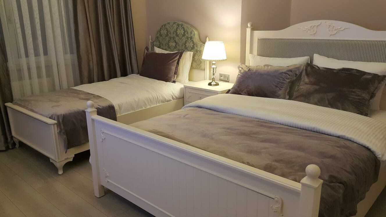 Habitación de hotel con dos camas, una mesita de noche con lámpara y una ventana con cortinas.