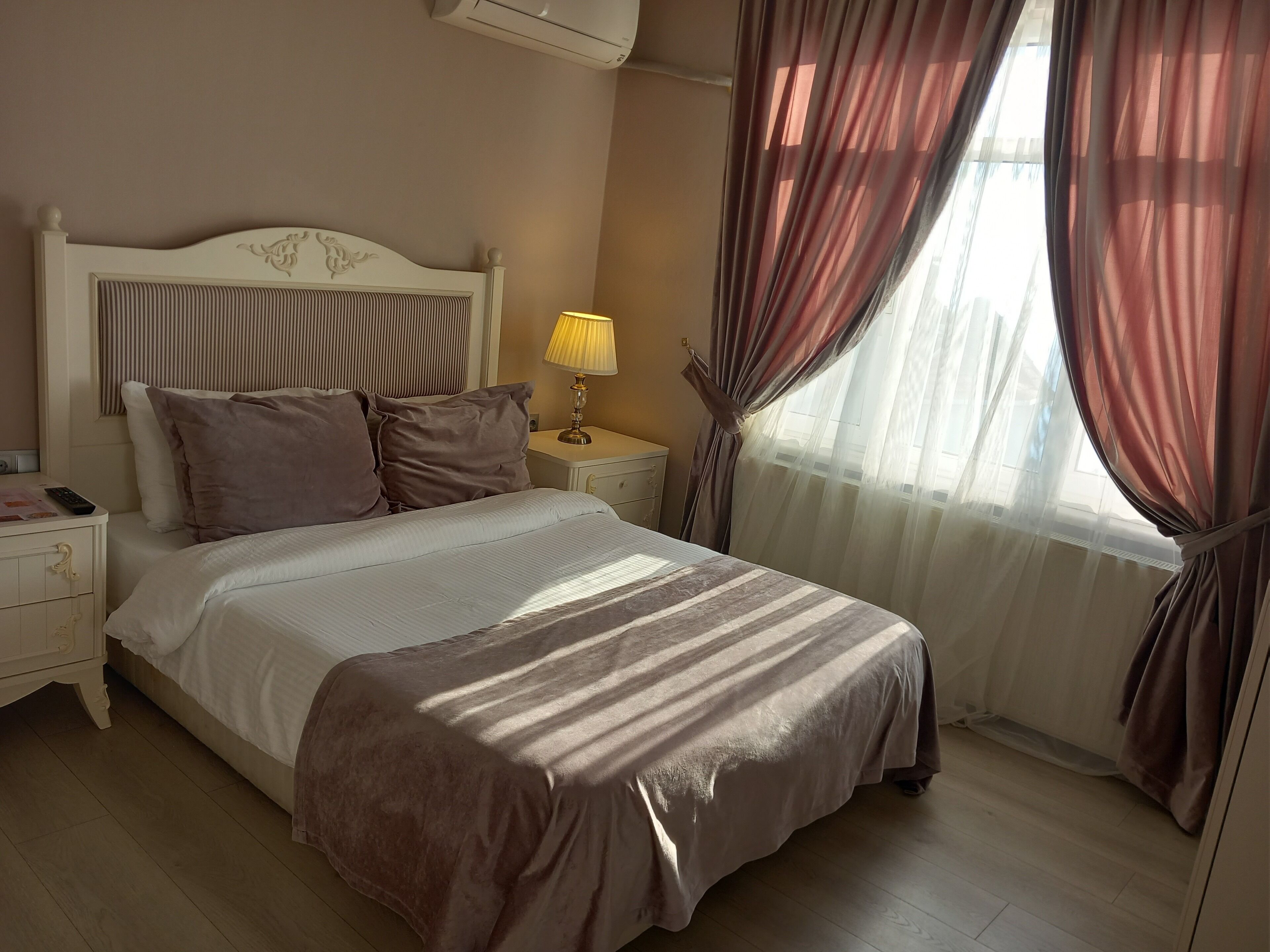 A neatly made bed with a headboard, a bedside lamp, and a nightstand with a phone and papers.