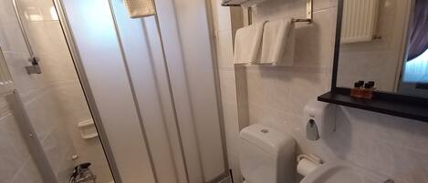 A modern bathroom with a glass shower enclosure, a toilet, a sink, and a towel rack with folded towels.