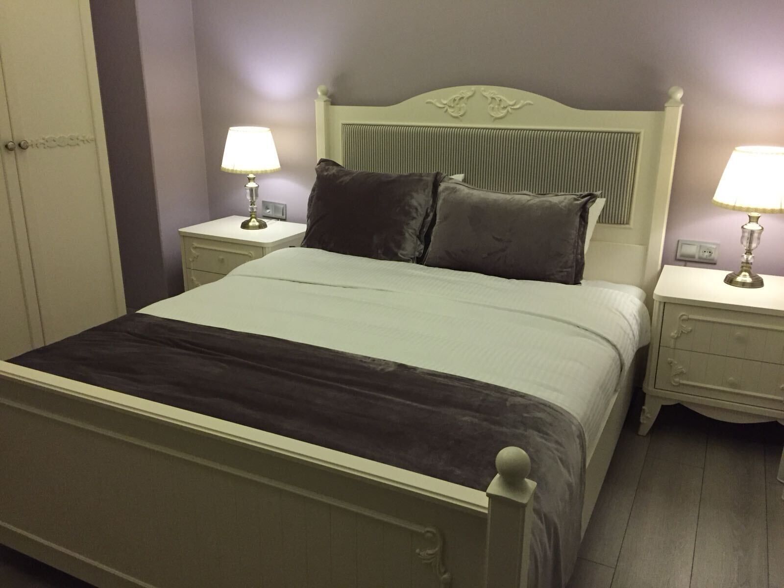 A bed with a headboard, two bedside tables with lamps, and a nightstand with a lamp.