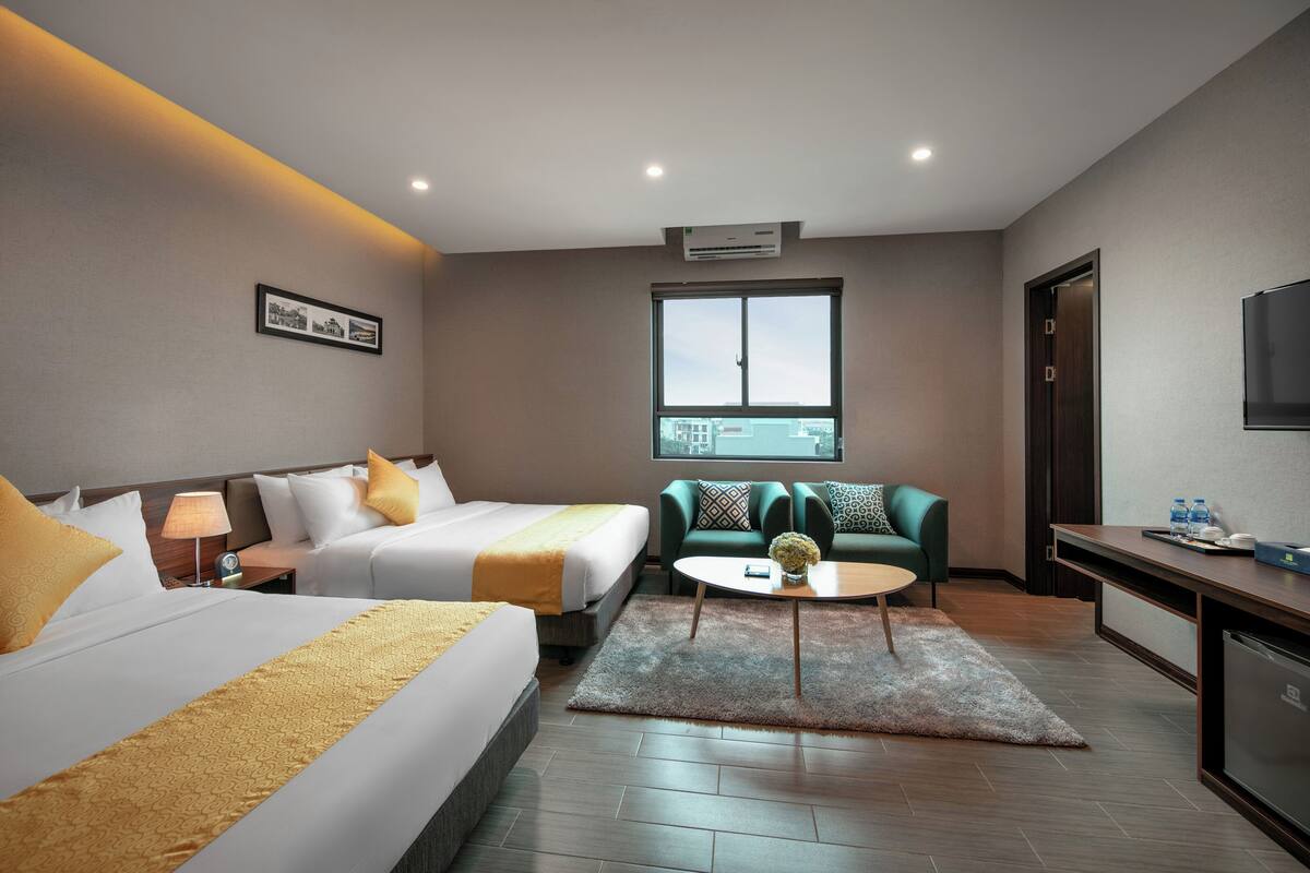 A hotel room with two beds, a sofa, a small table, and a TV.