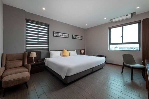 A hotel room with a bed, a chair, a nightstand, a lamp, a window, and a wall-mounted air conditioner.