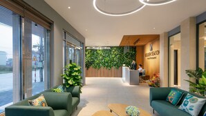 Un espace d’accueil moderne avec des canapés verts, un comptoir d’accueil en bois et un mur végétal.