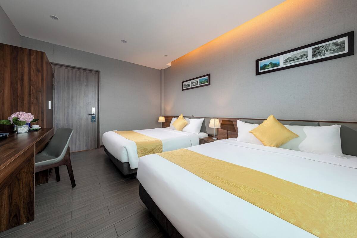 A hotel room with two beds, a desk, a chair, and a wooden wardrobe.