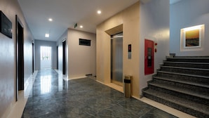 Un couloir moderne avec un sol en marbre, un ascenseur et un escalier.