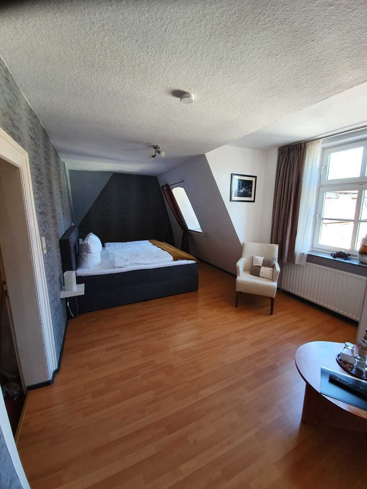 Ein Schlafzimmer mit einem Schlafpodest, einem Sessel, einem kleinen Tisch und einem Fenster mit Vorhängen.