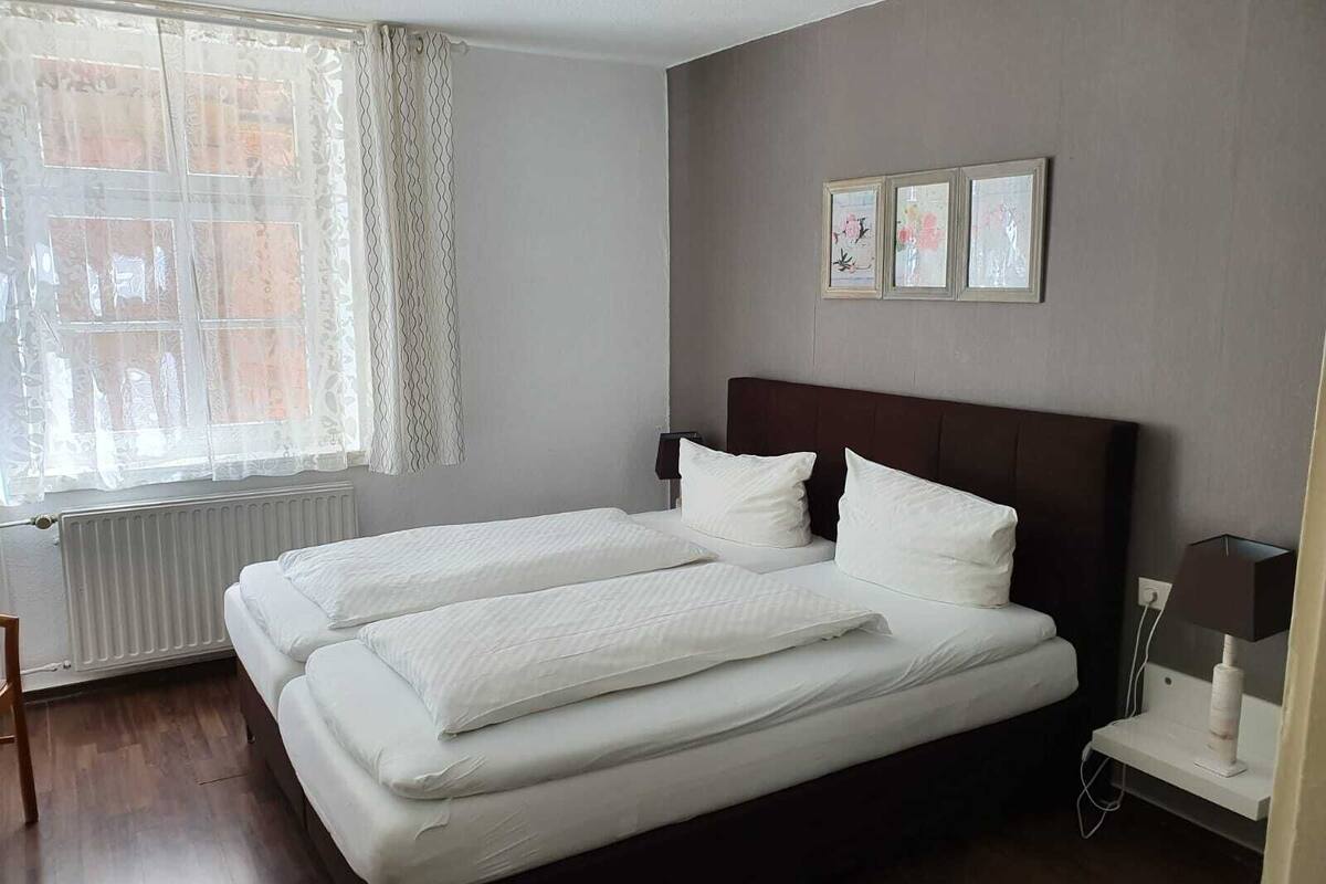 A double bed with white bedding, a headboard, and a bedside table with a lamp.