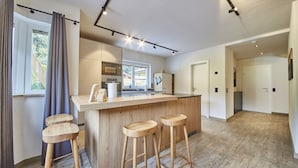 Una cocina moderna con una isla central, taburetes de bar, microondas y una ventana con cortinas.
