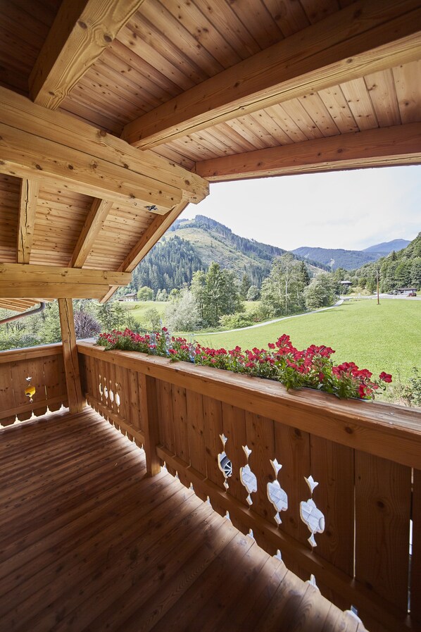 A wooden balcony with a view of a green field and mountains. - Holiday house / chalet with sauna, hot pot and home cinema - whole house (Viehhofen)