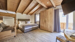 Un dormitorio con techo de madera, una cama con ropa de cama blanca y gris, un armario de madera y una mesita de noche con una lámpara.