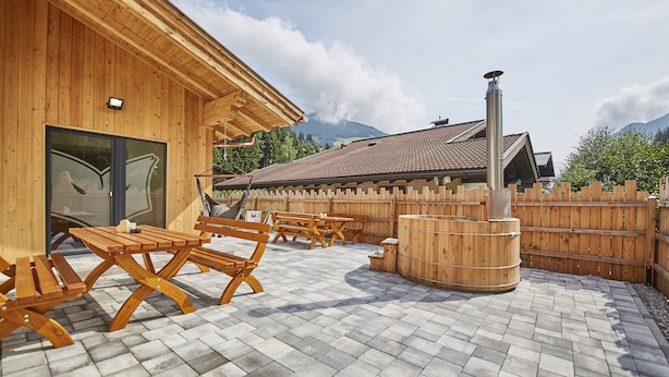 Edificio de madera con un patio que tiene bancos de madera y un barril de madera.