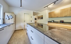 A modern kitchen with wooden cabinets, a granite countertop, and a view into the dining area. - Holiday house / chalet with sauna, hot pot and home cinema - whole house (Viehhofen)