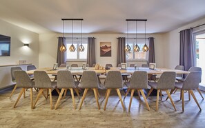 A conference room with a long table, grey upholstered chairs, wooden floors, pendant lights, and a mountain landscape painting. - Holiday house / chalet with sauna, hot pot and home cinema - whole house (Viehhofen)