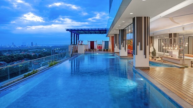 A modern rooftop pool area with a city view, a bar, and a covered seating area. - Aston Gresik Hotel & Conference Center (Gresik)