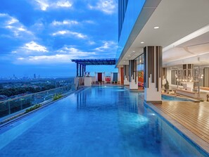 A modern rooftop pool area with a city view, a bar, and a covered seating area.