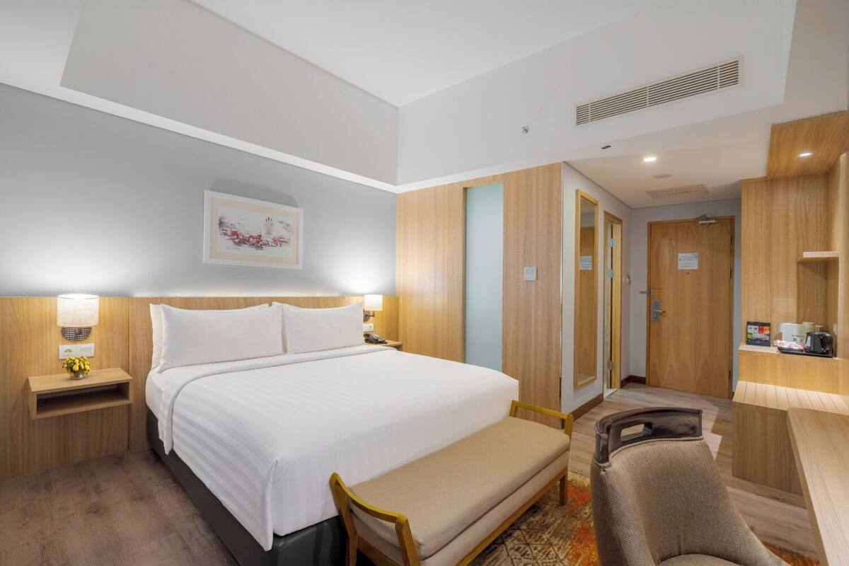 Una habitación de hotel con una cama grande, mesitas de noche, un escritorio, una silla y un armario.