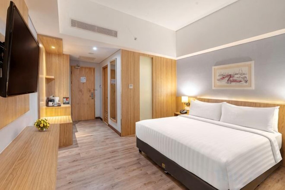 A hotel room with a bed, bedside table, lamp, TV, and a door leading to a bathroom.