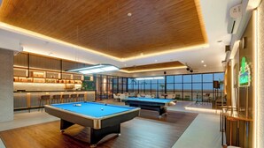 A modern indoor pool area with two pool tables, a bar area, and a seating area with a view of the outdoors. - Aston Gresik Hotel & Conference Center (Gresik)