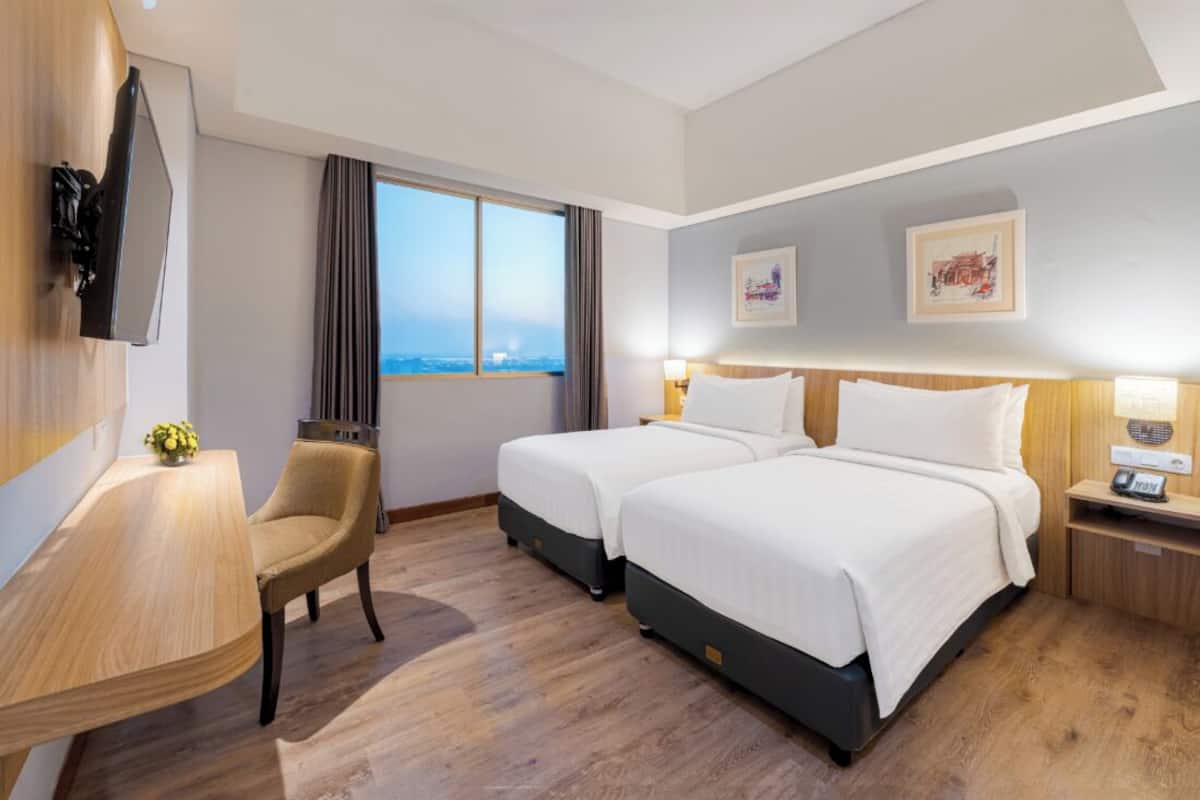 Habitación de hotel con dos camas, un escritorio, una silla, un televisor y una ventana con vistas.
