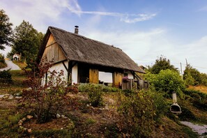 Une maison traditionnelle à toit de chaume, aux murs blancs, entourée d’un paysage naturel composé d’arbres et d’arbustes.