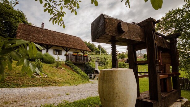 A traditional thatched-roof house with a stone well and a wooden structure with a large stone basin.