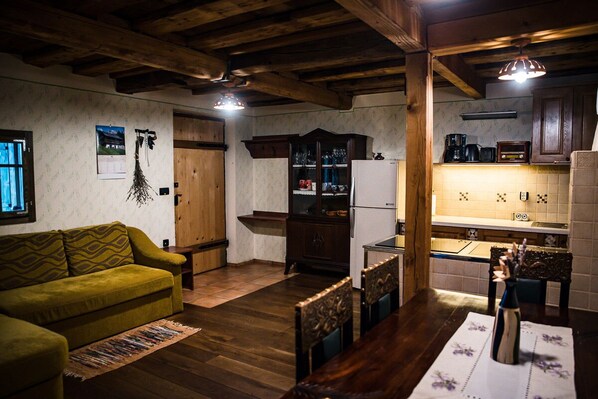 A cozy living room with a sofa, wooden dining table, chairs, and a kitchen area with cabinets and appliances. - Vineyard cottage Škatlar 2 (Otočec)